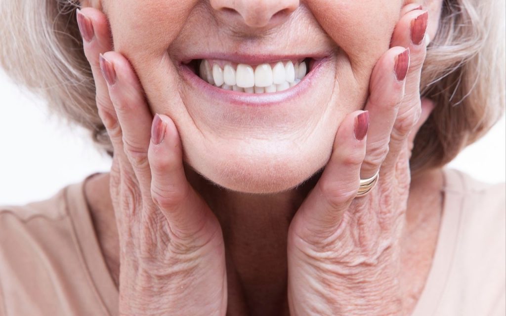 An older woman smiling with her hands on her face, showcasing denture stains.