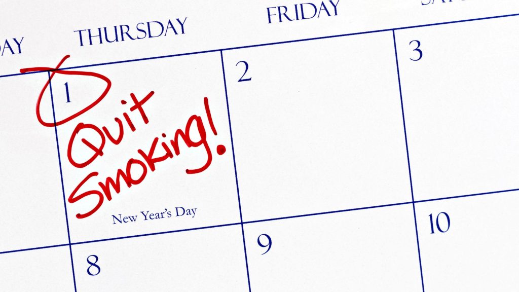 A closeup of a calendar showing January 1st with "Quit Smoking!" written in red marker, indicating a New Year's resolution.