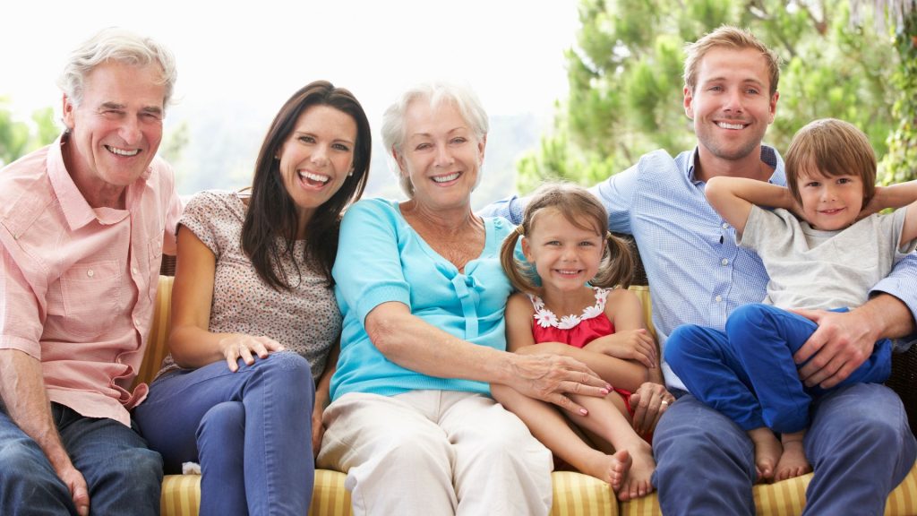 Canadian Dental Care Plan - Three adults and three children sit closely together on an outdoor bench, smiling at the camera, with green trees in the background—enjoying family time and peace of mind thanks to the Canada Dental Care Plan (CDCP).