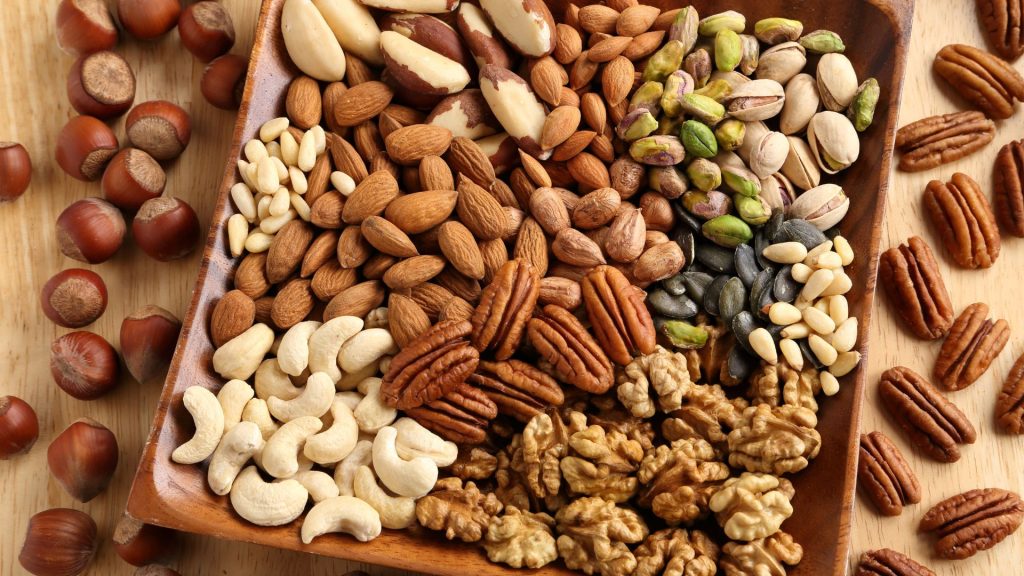 A wooden tray filled with assorted nuts—including almonds, pecans, cashews, and walnuts—showcases popular foods that crack teeth and can lead to tooth fractures if not eaten carefully.