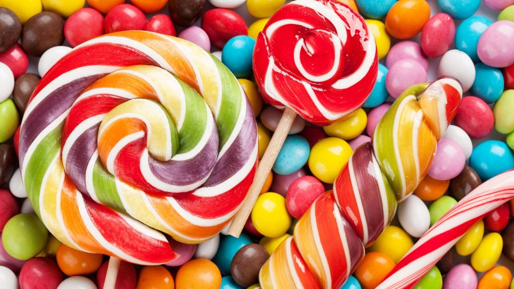 Assorted colorful lollipops and candy-coated chocolates arranged closely together, featuring swirled and twisted designs—some are classic foods that crack teeth if enjoyed too eagerly.