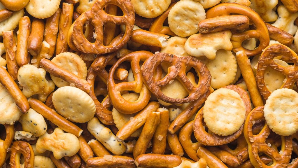 A close-up view of an assortment of salty snacks, including pretzels, crackers, and breadsticks—hard foods that damage teeth and can lead to cracked teeth if eaten carelessly.