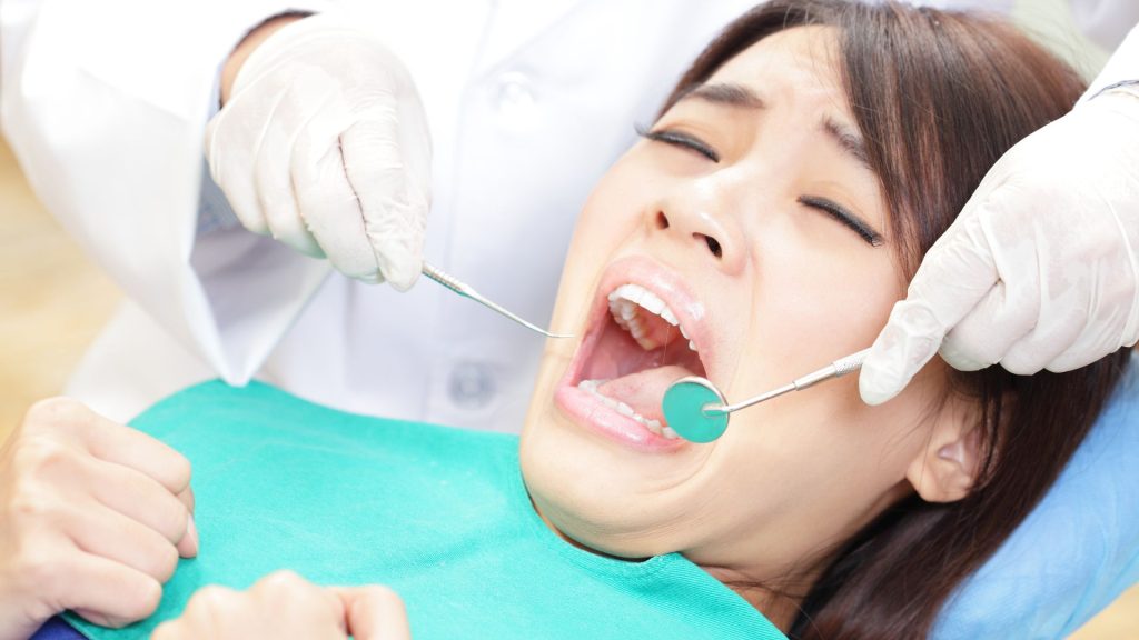 Why avoiding the dentist can make things worse. A patient with an anxious expression receives a dental examination from a dentist using dental tools while lying in a dental chair.