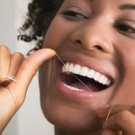 A person smiling while using dental floss to clean their teeth.