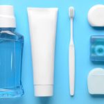Mouthwash, toothpaste, toothbrush, and three types of dental floss arranged neatly on a blue background.